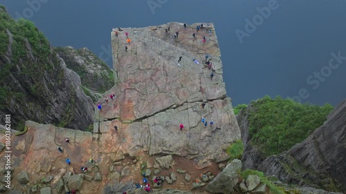 Tourists enjoy Pulpit Rock cliff Preikestolen Norway. Visitors sit and walk across the famous rock formation, enjoying the dramatic drop and peaceful scenery during a summer hike.