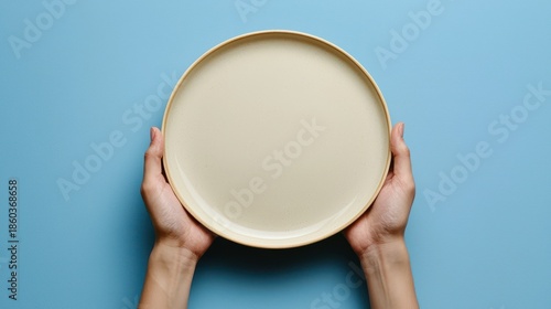 Empty Round Plate Held by Hands Against a Blue Background in a Minimalistic Style for Culinary and Restaurant Themes