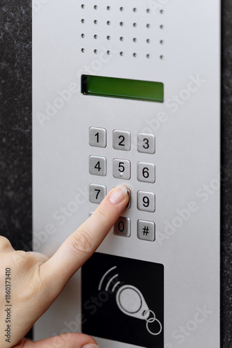 Close-up of a hand pressing a button on a modern intercom keypad mounted on a dark textured wall.