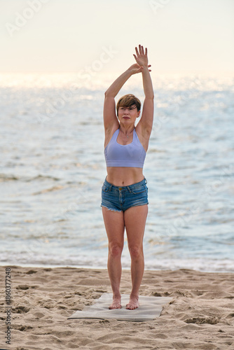 Young woman practicing yoga stretch on Baltic Sea beach at sunrise
