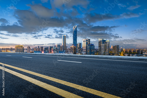 Empty asphalt road and modern city skyline at sunset.