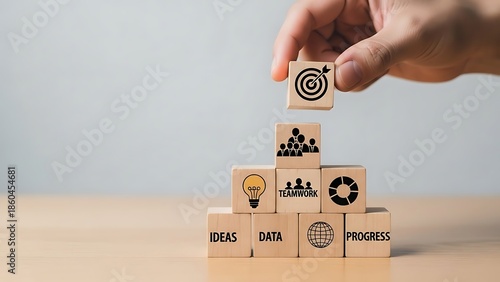 A hand carefully places a block with a target on top of a wooden block tower representing business goals and