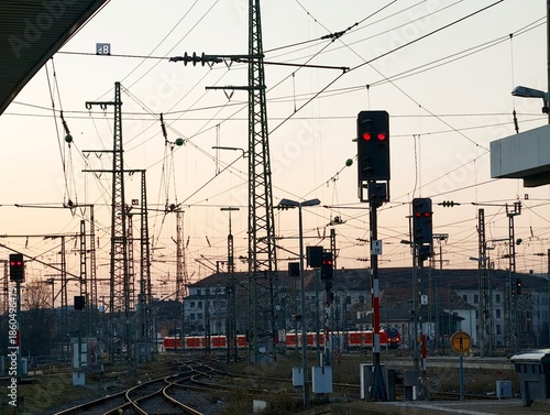 Railway infrastructure with tracks, overhead power lines, and red signals at sunset
