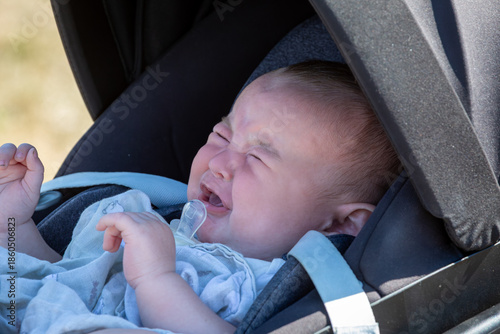 A close-up of a crying baby in a car seat. This authentic lifestyle image captures a common moment of infant distress or discomfort, highlighting the challenges of parenting and travel.