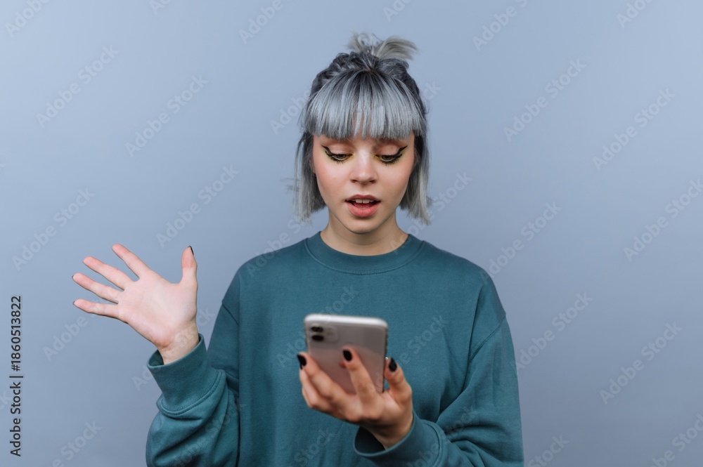 Fototapeta premium Young woman with gray hair looking surprised at smartphone.