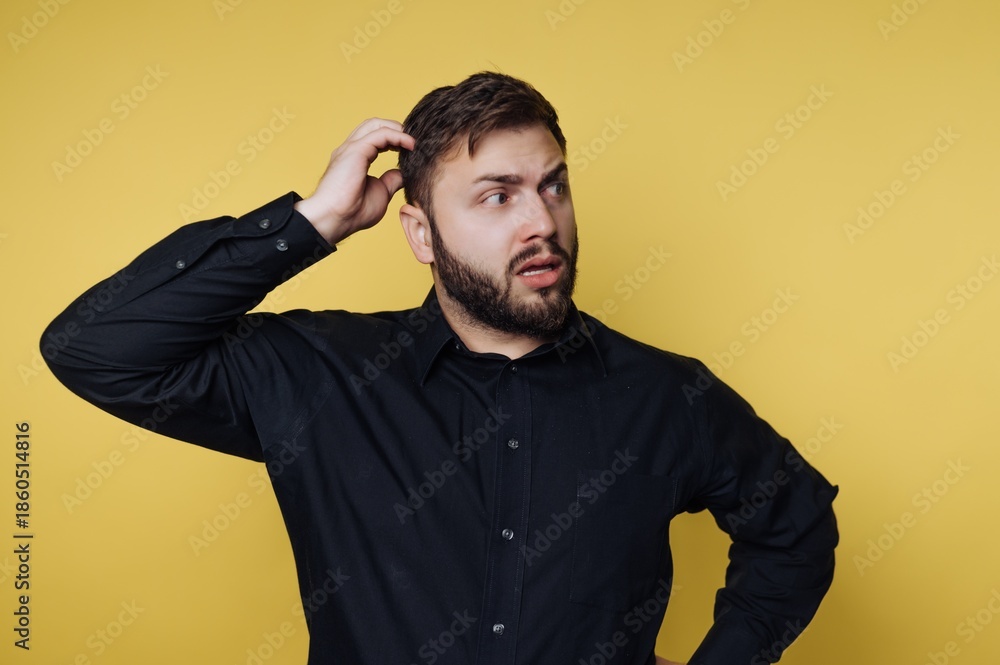Fototapeta premium Man in black shirt scratching head against yellow background.