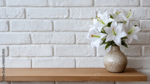 Artificial lily flowers arranged in a vase on a shelf beside a white brick wall, creating a clean decorative accent.

