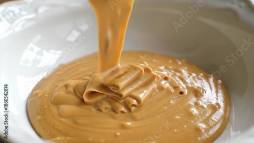 A smooth, creamy paste is being poured into a white bowl, creating a swirly pattern