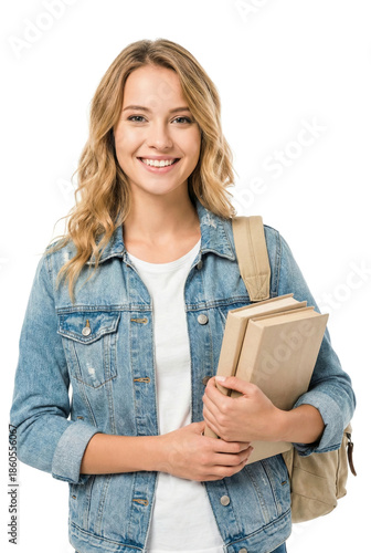 Woman stands isolated with books in her arms and smiles at the camera.