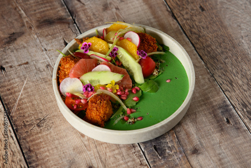 A white bowl with a green sauce and a variety of vegetables including carrots