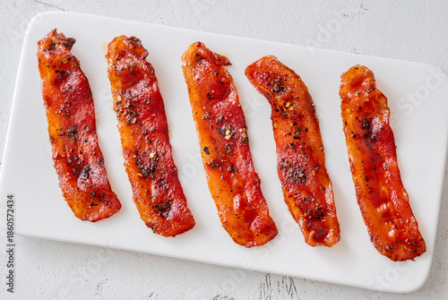 Billionaire bacon strips glazed with pepper and chili flakes on minimalist plate