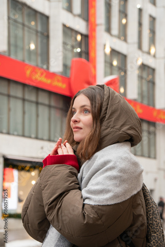 Fotografie Woman in winter coat and scarf stands on wet street near decorated facade and en