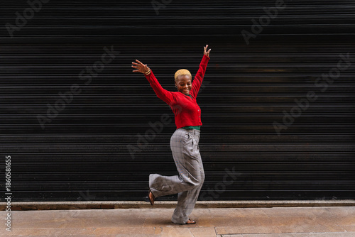 Happy young black woman dancing in front of a contrasting black background feeling joyful