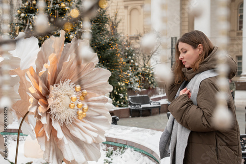 Woman walks near a snow-covered fountain with large white New Year flower installation in front of the Bolshoi Theatre