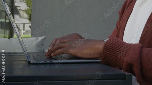 Black woman's hands typing on laptop keyboard outdoors