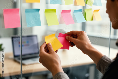 Hands adding sticky note to glass team workflow board.