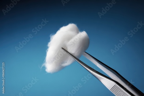 Macro shot of metal tweezers holding fluffy white cotton ball against blue background tool instrument