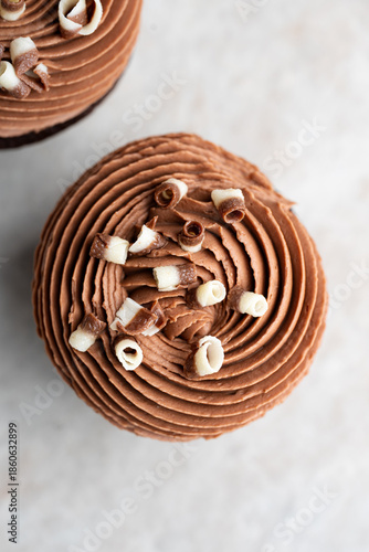 Chocolate cupcake with swirled cream cheese frosting with chocolate curls top view, a minimal high-key dessert on a white stone background.