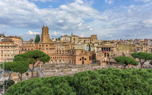 Rome, Italy. Panoramic view of ancient Roman ruins and historic buildings, showcasing lush greenery and vibrant city life with dramatic clouds overhead