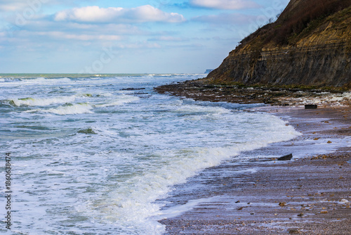 Waves crashing against the cliff at high tide in Port-en-Bessin