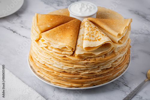 Stack of golden crepes served with sour cream