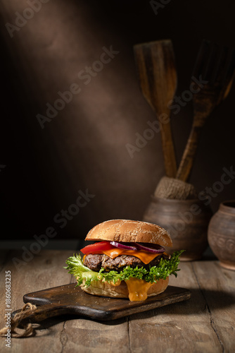 Homemade hamburger on a wooden cutting board against a dark wall