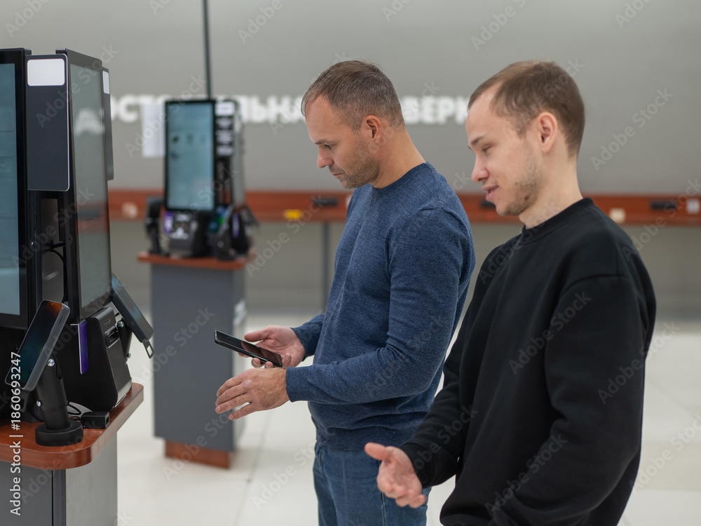 Fototapeta premium Two Caucasian men use a self-checkout machine at a hardware store.