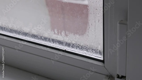 Heavy condensation with water droplets forms on a cold glass window pane. The camera slowly zooms in, showing moisture from high indoor humidity during cold winter weather.