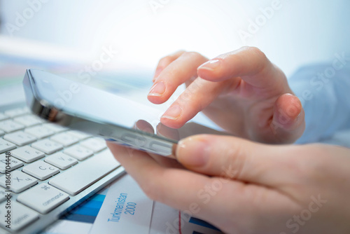 A woman works with a smartphone in the office, on a report. Close-up of her hands. 	