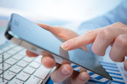A woman works with a smartphone in the office, on a report. Close-up of her hands. 	