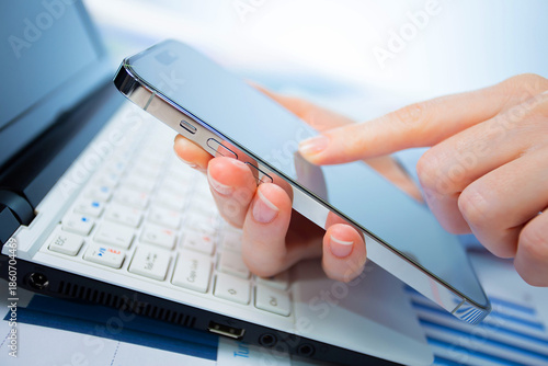 A woman works with a smartphone in the office, on a report. Close-up of her hands. 	