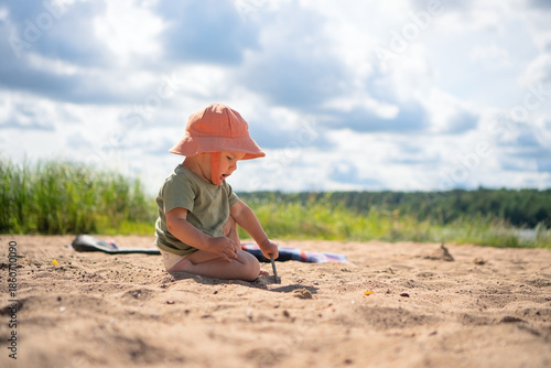 A toddler plays on a sandy beach wearing an orange hat, enjoying the warmth and freedom of outdoor play.