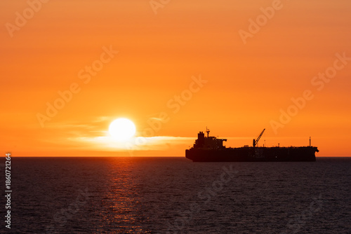 Silhouette of a fuel tanker ship sailing on the horizon of the Baltic Sea near Estonia during a vibrant orange sunset