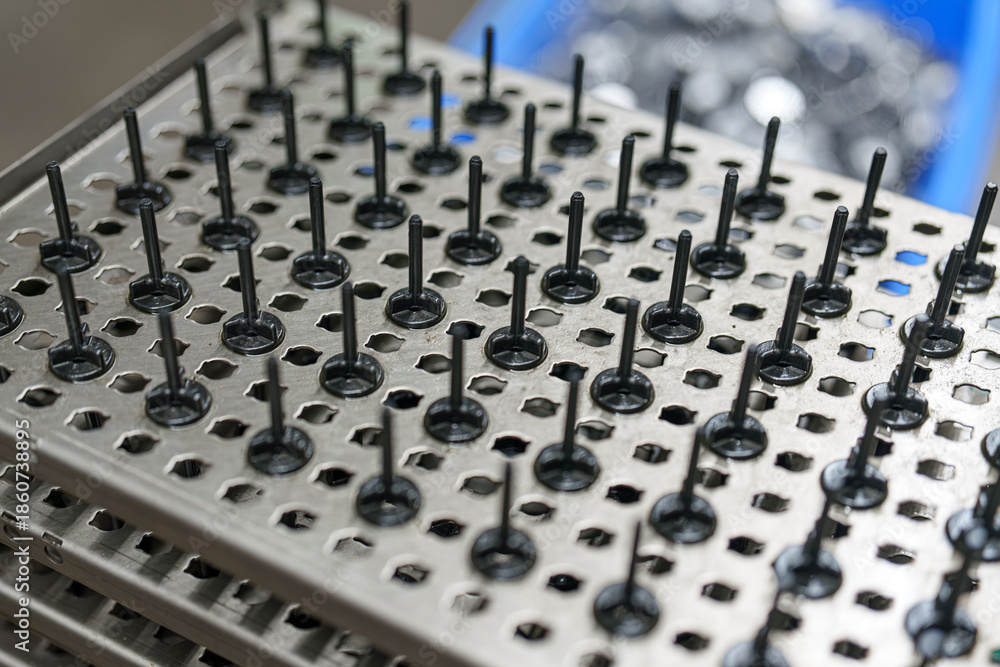 Obraz premium Metal tray holds several black pins arranged neatly in rows at a manufacturing facility during a workday