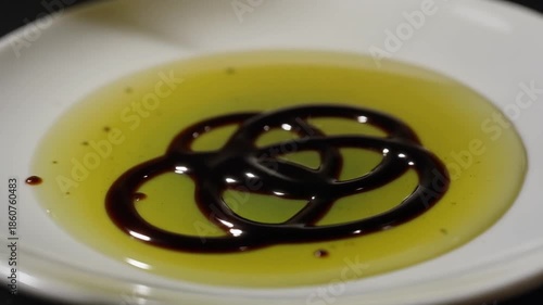 Olive oil and balsamic vinegar artfully drizzled in an intricate circular pattern on a white plate, creating a visually appealing culinary presentation.