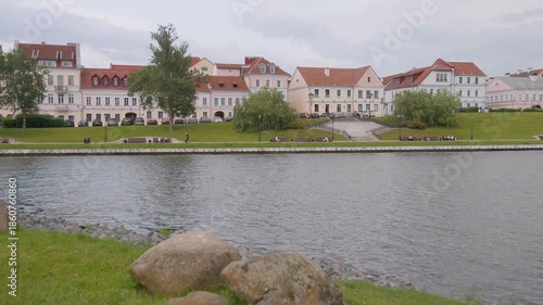 Beautiful historic buildings of the trinity suburb along the svislach river embankment in minsk, belarus, with a green park and people relaxing on benches on a cloudy day in eastern europe