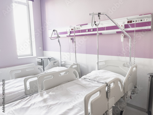 Bright and modern sick room with two empty medical beds in a horizontal orientation, purple walls and natural daylight coming through the window