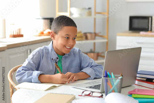 Little African-American boy studying computer sciences online in kitchen