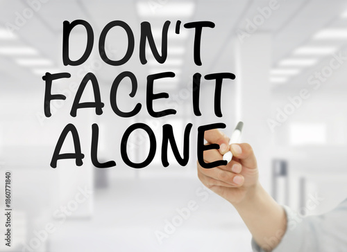 Wallpaper Mural A conceptual business image showing "Don't face it alone" handwritten in bold black letters on transparent glass, with a blurred modern white office interior in the background.  Torontodigital.ca