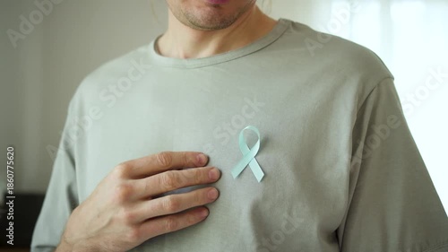 A young man pins a blue satin ribbon to his shirt for November Prostate Cancer Awareness Month, supporting diagnosis, treatment, and patient community.