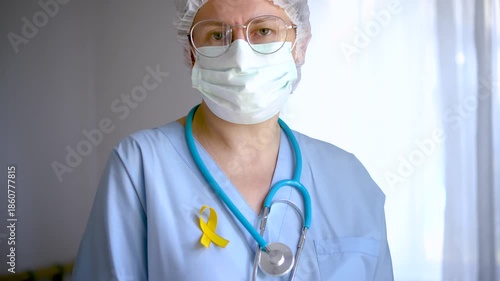 A woman medical staff holds a yellow satin ribbon, emblem for sarcoma, childhood cancer, suicide prevention, endometriosis and liver disease awareness.