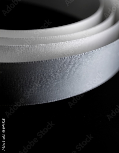 Close-up of a shimmering silver satin ribbon coiled against a dark background, highlighting its smooth texture and elegant sheen.