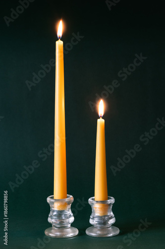 Photography Two yellow beeswax taper candles burning in glass candle holders on dark green b
