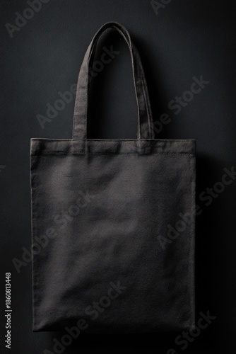 Black tote bag on black backdrop. Simple, minimalist design, vertical shot