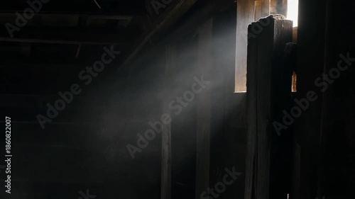 Atmospheric light ray piercing through a dark, dusty room with wooden structures.
