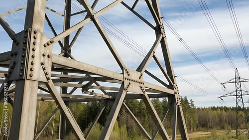 Close-up of Power Line Tower Structure with Blue Sky and Green Trees