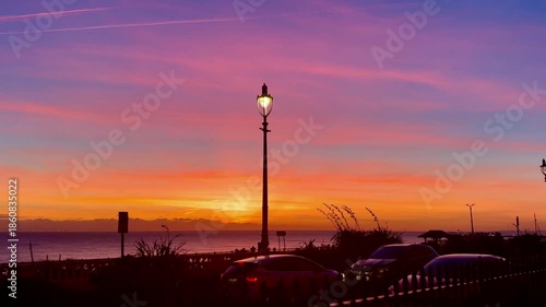 beautiful sunset over seafront with street lamp and cars passing in foreground