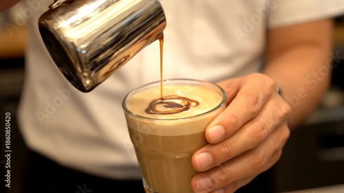 Barista pouring chocolate sauce into a latte, creating coffee art in a glass