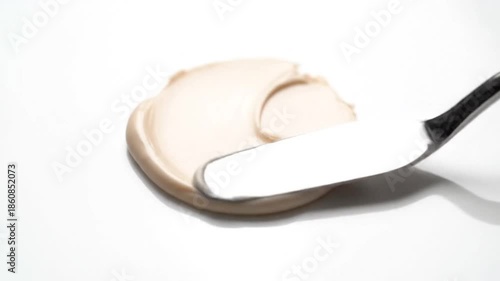 Close-up of beige cream spread on white, with spatula scraping surface
