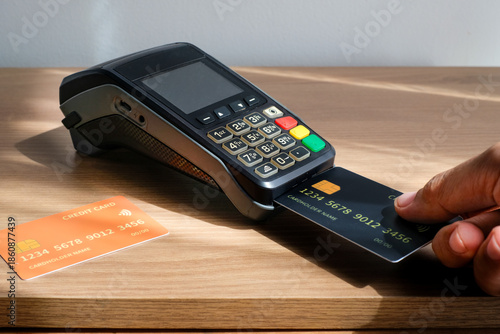 Hand inserting a credit card into an electronic EDC terminal on a wooden desk.Perfect for fintech marketing, payment solutions, ecommerce, business finance content, modern retail transaction, cashless
